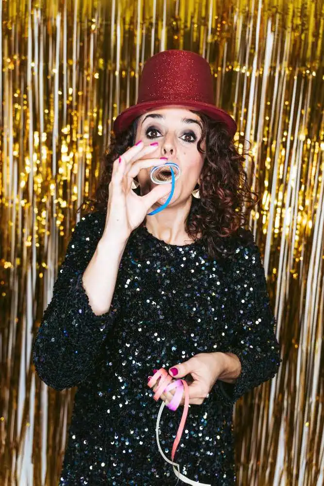 woman-in-a-red-top-hat-and-sequined-dress-celebrating-with-a-party-blower-against-a-gold-backdrop